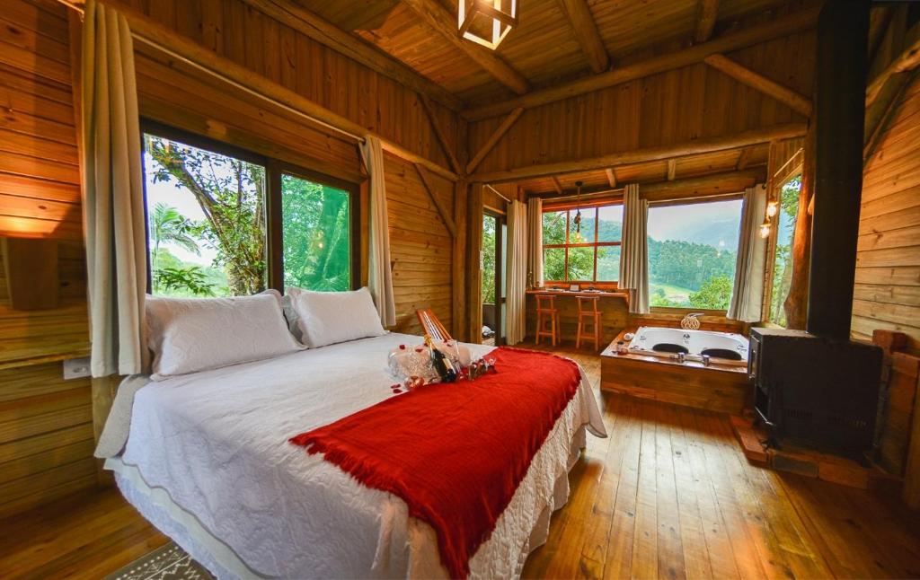 Visão interna de uma cabana no glamping, com cama de casal e janela com vista para a natureza