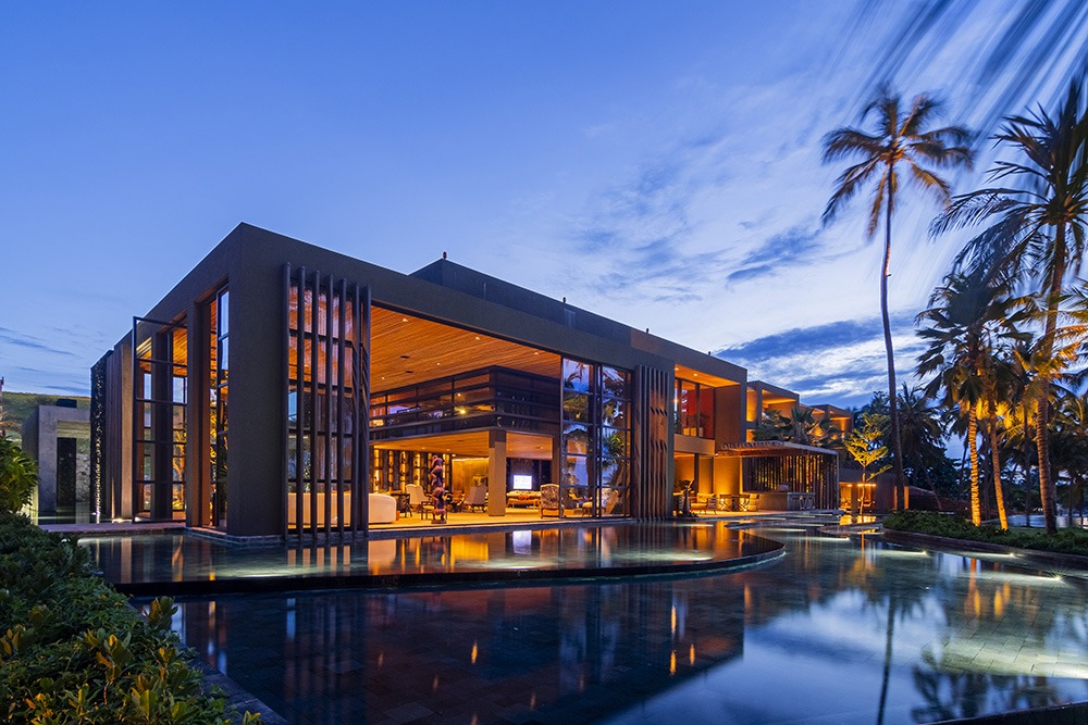 Vista da fachada do resort, com piscina na frente e palmeiras ao redor.