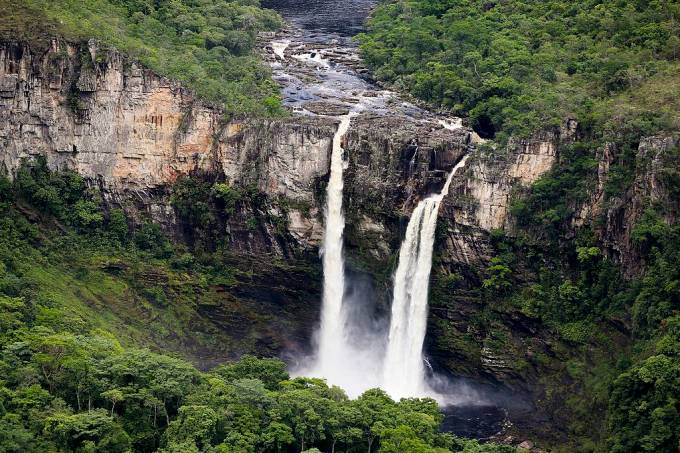 Imagem panorâmica, vista de cima, de uma cachoeira no Parque Nacional da Chapada dos Veadeiros, com grande vegetação em volta.