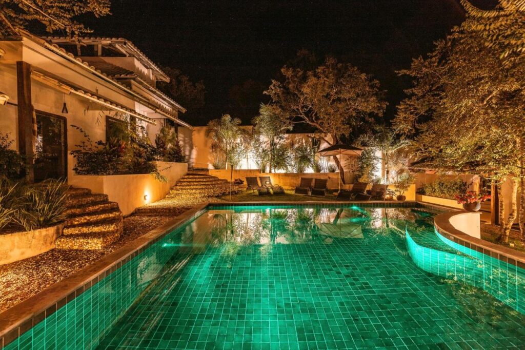 Vista da piscina na parte externa da pousada de luxo na Chapada dos Veadeiros chamada Casa de Shiva, com piscina e ambiente arborizado, à noite.